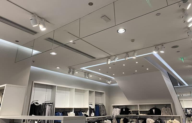 Modern clothing store interior with bright recessed downlight and track lighting illuminating apparel displays.