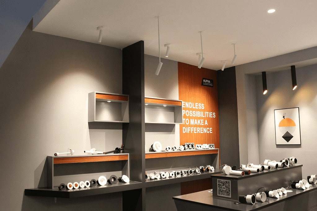 Modern lighting showroom with various recessed downlight and track light fixtures displayed on dark shelves.