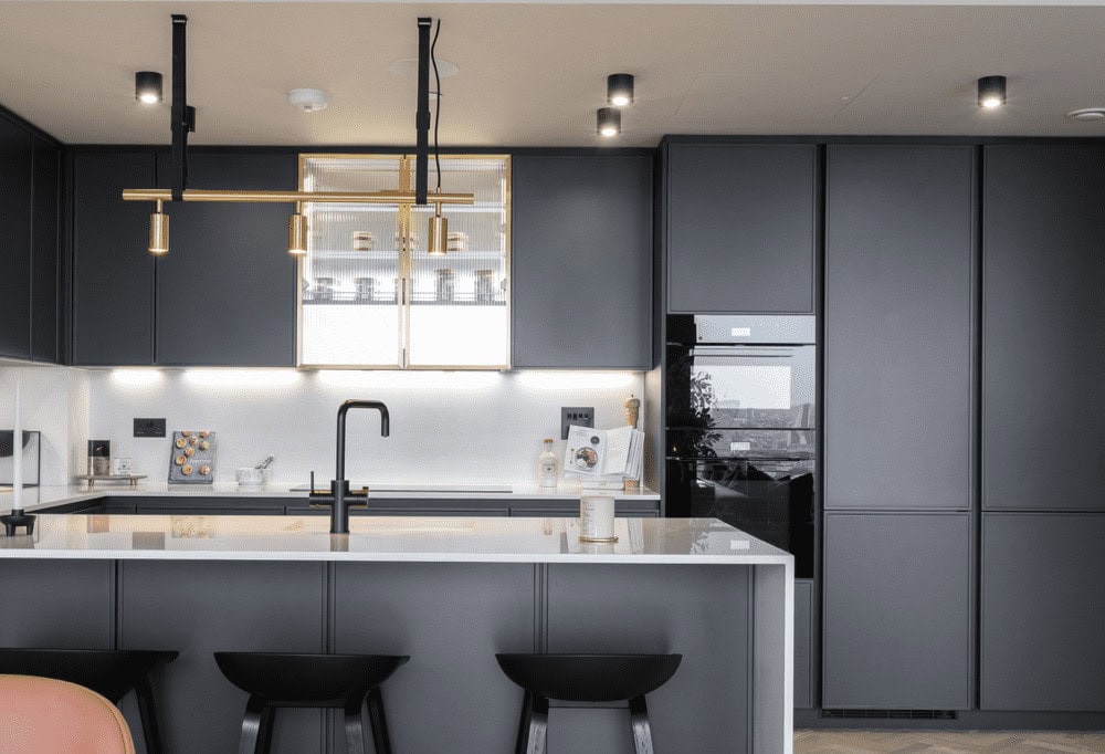 Sleek dark kitchen with recessed downlight, under-cabinet lighting, and brass pendant fixtures.