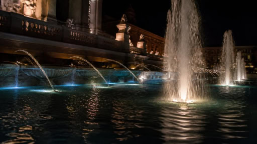 Underwater fountain lights illuminate multi-jet fountain beside classical buildings at night